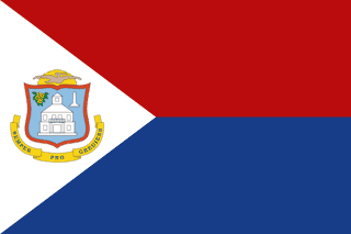 The flag of Sint Maarten features two equal horizontal bands of red and blue, with a white isosceles triangle based on the hoist side. The center of the triangle displays the national coat of arms with an orange-bordered blue shield that prominently displays a white courthouse, as well as yellow sage in the upper left and the silhouette of a monument in the upper right. Over the shield is a yellow rising sun and a brown pelican in flight. A yellow scroll below the shield has the Latin motto "SEMPER PROGREDIENS" (Always Progressing).