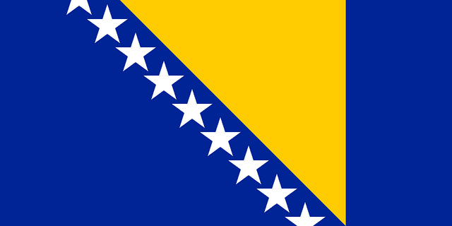 The flag of Bosnia and Herzegovina has a blue field, at the center of which is a large yellow hoist-side facing right-angled triangle that is based on the top edge and spans the height of the field. Adjacent to the hypotenuse of this triangle are nine adjoining five-pointed white stars with the top and bottom stars cut in half by the edges of the field.