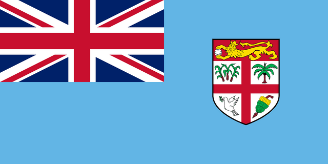 The flag of Fiji has a light blue field. It features the flag of the United Kingdom — the Union Jack — in the canton and the shield of the national coat of arms centered in the fly half.
